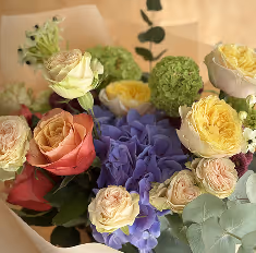 Bouquet of mixed flowers including yellow roses, pink and cream roses, purple hydrangeas, and green foliage.