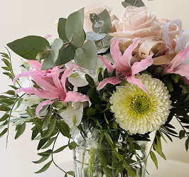 Bouquet of mixed flowers including pink lilies, white chrysanthemum, and pale pink roses in a glass vase.