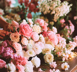 Armful of various pink and white flowers arranged on a table with hands gently touching them.