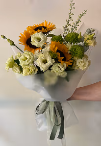 Bouquet of sunflowers, white and green flowers wrapped in translucent paper with green ribbons held by a hand.