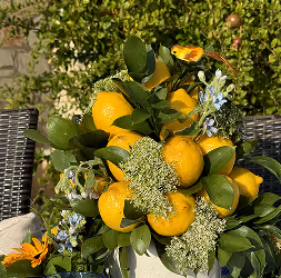 Bouquet of bright yellow lemons with green leaves and small white and blue flowers arranged outdoors.
