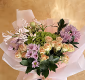 Bouquet with light pink roses, purple flowers, and green foliage wrapped in pale pink translucent paper.