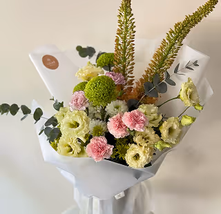 Bouquet of pink carnations, green chrysanthemums, white lisianthus, and eucalyptus wrapped in white paper.