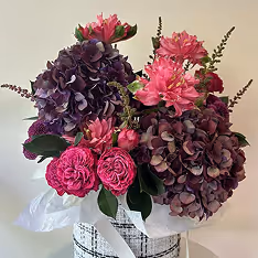 Bouquet of purple hydrangeas mixed with bright pink flowers arranged in a white and black patterned vase with white tissue paper.