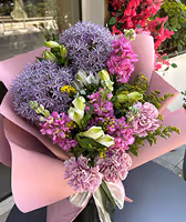Bouquet of purple alliums, pink carnations, and small pink and white flowers wrapped in pink paper.