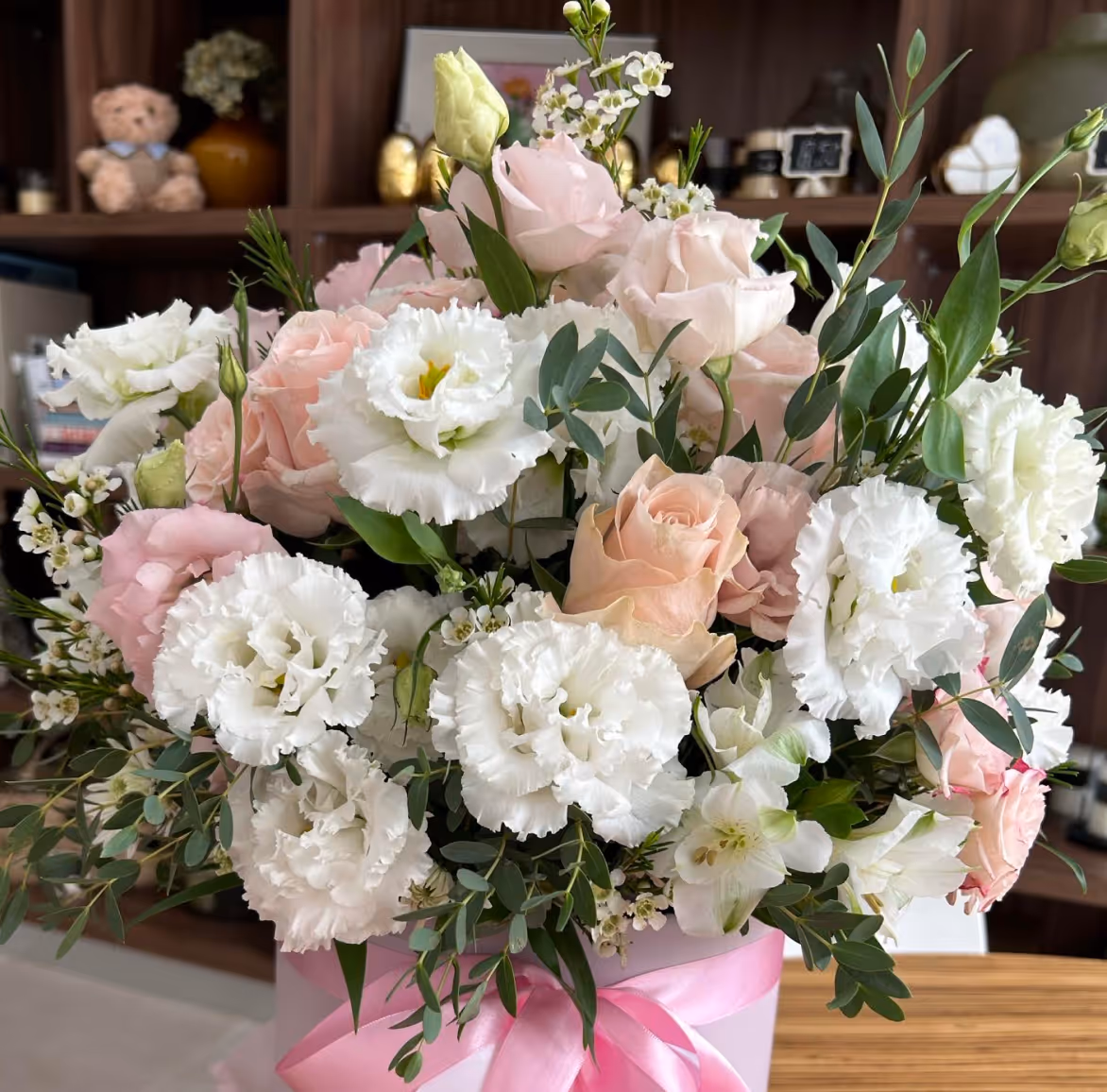 Bouquet of white and pale pink flowers with green leaves in a pink box with ribbon.