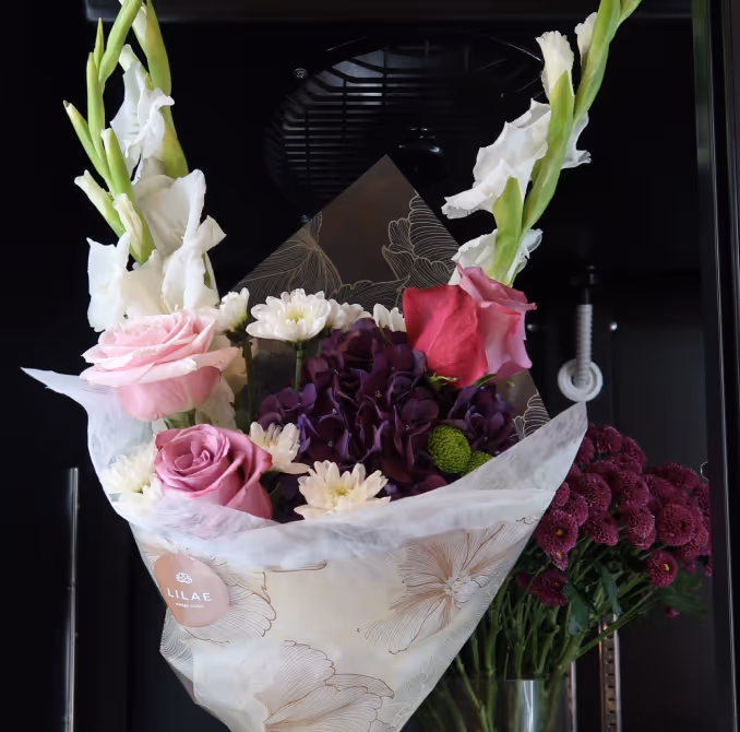 Bouquet of pink roses, white gladiolus, purple hydrangeas, and small white flowers wrapped in decorative paper.