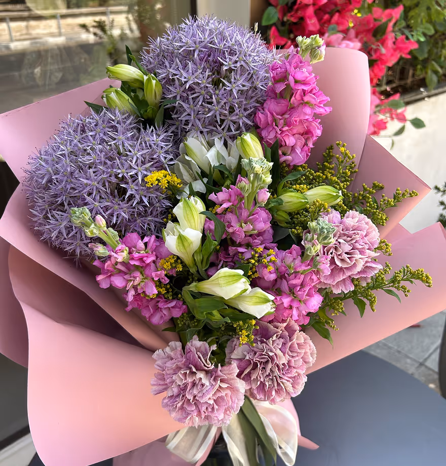Bouquet with purple allium, pink carnations, white and pink flowers wrapped in pink paper.