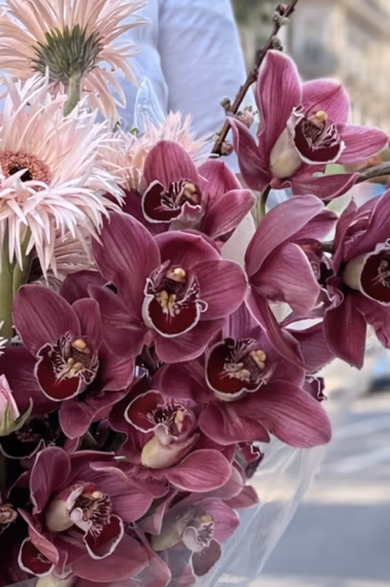 Bouquet of dark pink orchids and pale pink spiky flowers held in hand outdoors.