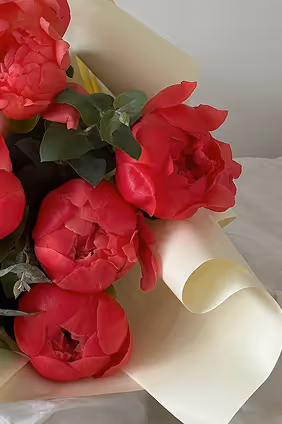 Close-up of a bouquet with vibrant red peony flowers wrapped in light cream paper.