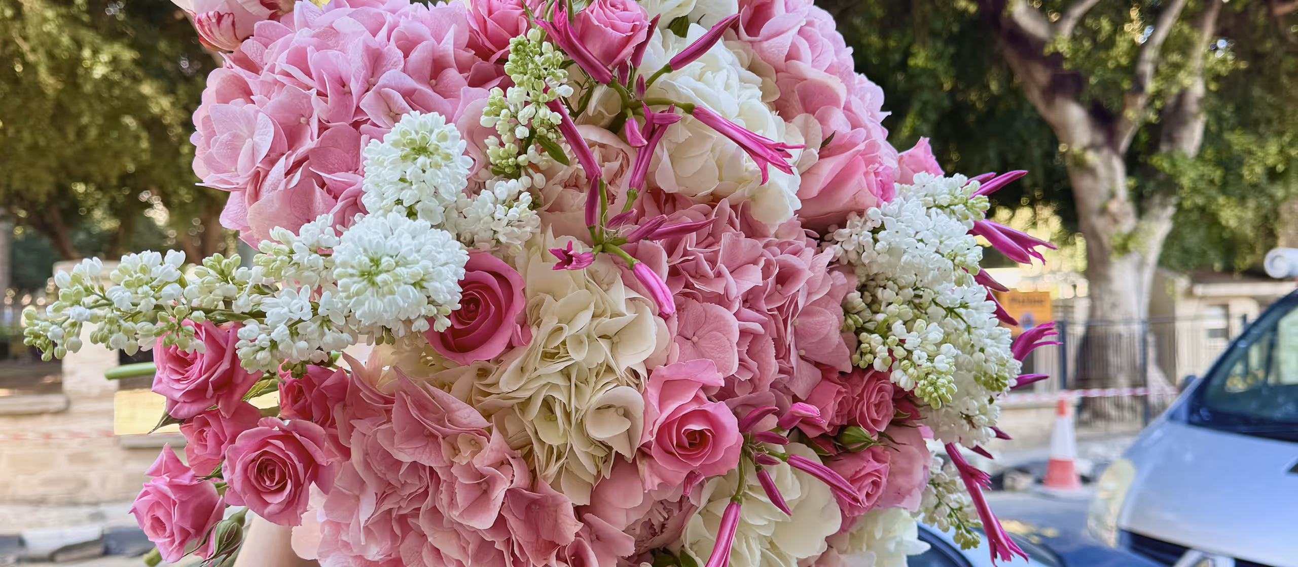 Close-up of a bouquet of pink and white flowers including roses, hydrangeas, and lilacs outdoors.