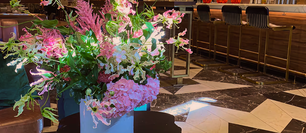 Bright floral arrangement with pink and green flowers in a gray vase on a black table in a modern restaurant interior.
