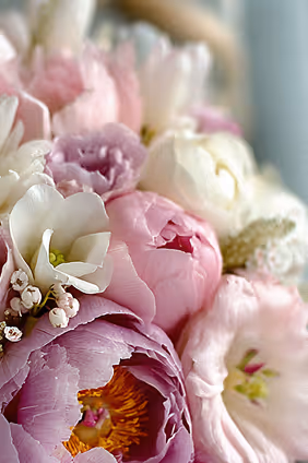 Close-up of a bouquet with soft pink and white flowers, including peonies and lilies.