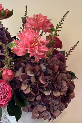 Arrangement of pink and purple flowers including hydrangeas and azaleas against a light background.
