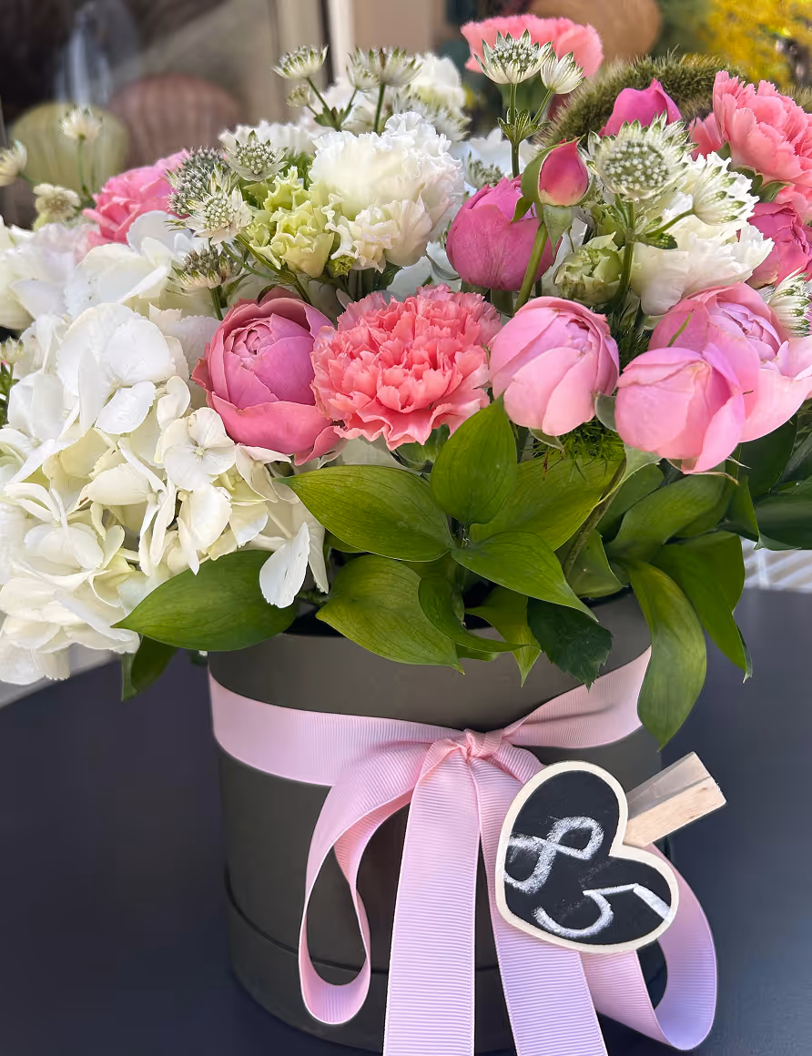 Flower arrangement in a black hatbox with pink ribbon and heart-shaped tag reading 85.