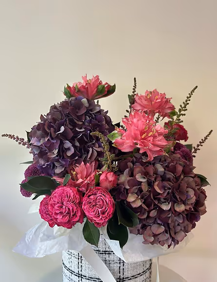 Bouquet of purple hydrangeas and pink roses arranged in a white and black checkered basket.