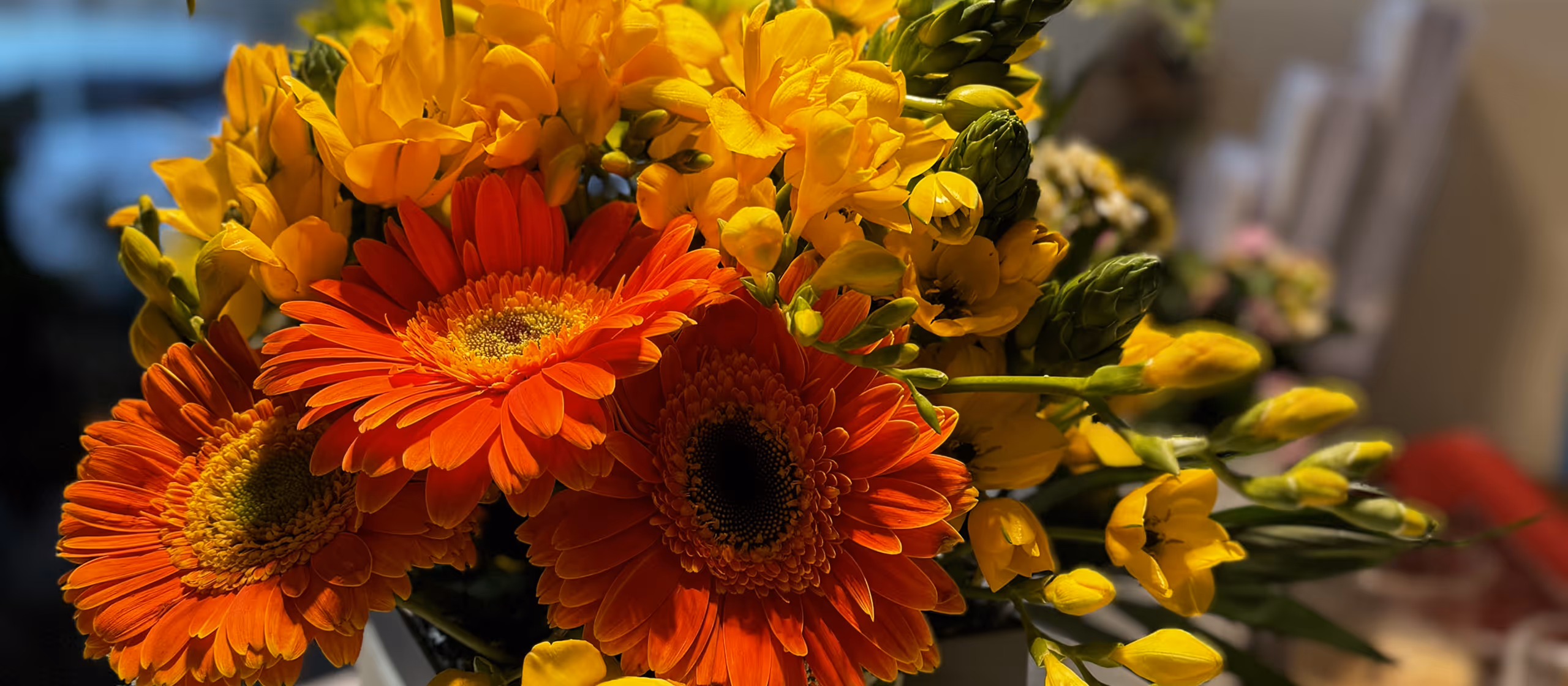 Close-up of a bouquet with bright orange gerbera daisies and small yellow flowers indoors.