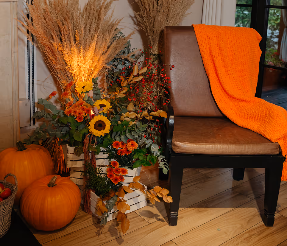 Decorative arrangement with sunflowers, pumpkins, fall leaves, and a chair draped with an orange blanket.