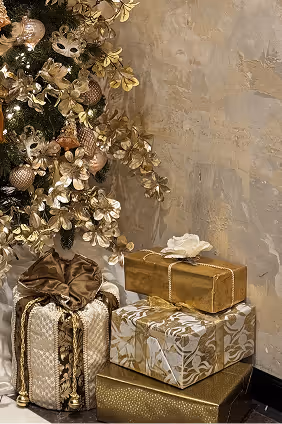 Gold and white wrapped gifts beneath a gold-themed decorated Christmas tree with lights and ornaments.