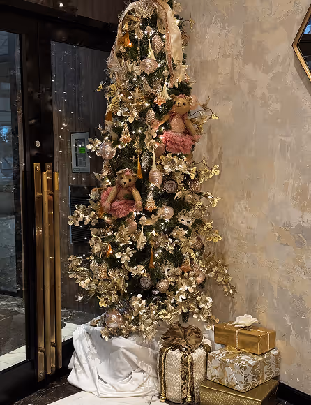 Tall Christmas tree decorated with gold flowers, teddy bears, ornaments, ribbons, and gifts underneath.