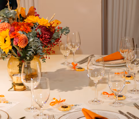 Elegant dining table with autumn-themed floral centerpiece, orange napkins, and multiple wine glasses.