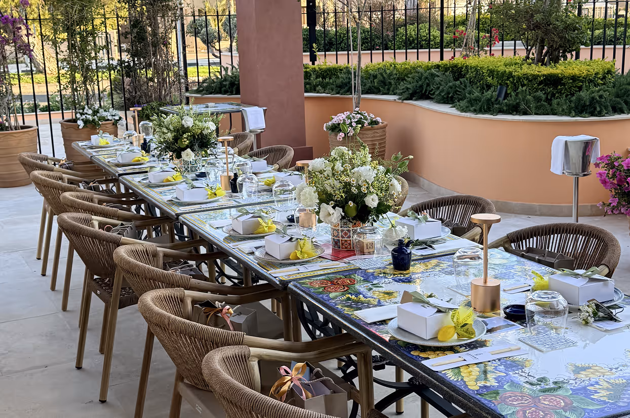 Outdoor dining table with floral centerpieces, boxed favors, and wicker chairs on a patio.