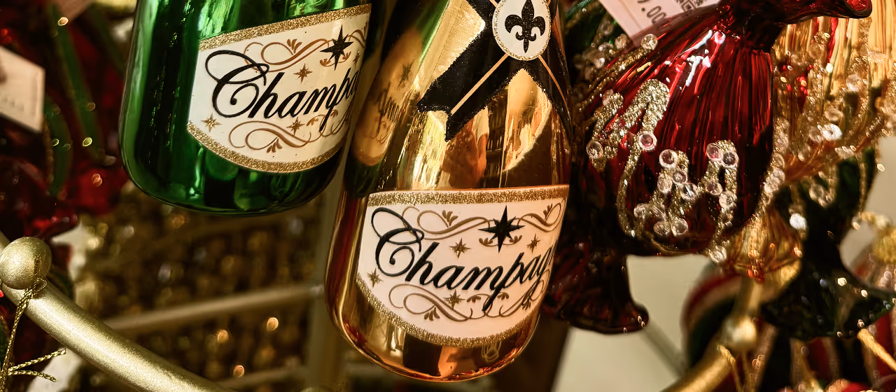 Close-up of green and gold champagne bottle toys ornaments hanging among other festive holiday decorations.