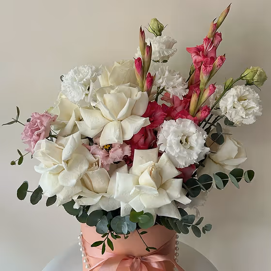 Bouquet of white roses, pink and white lisianthus flowers with green eucalyptus leaves in a pink vase tied with a ribbon and pearls.