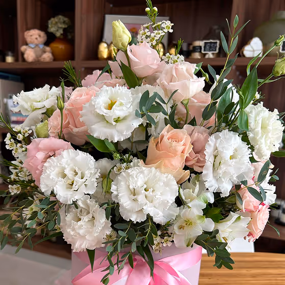 Bouquet of pink and white roses and white lisianthus flowers in a pink vase with a pink ribbon.