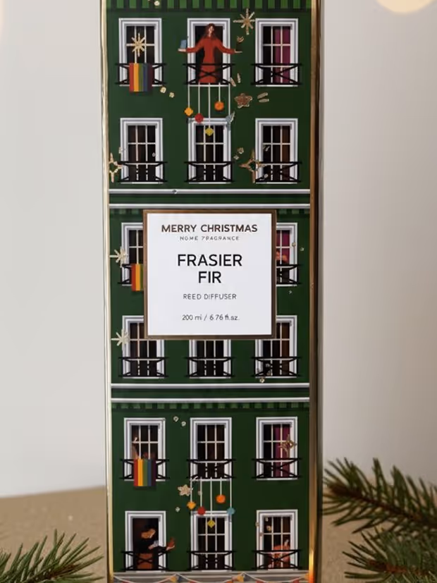 Green rectangular box of Merry Christmas Frasier Fir reed diffuser with illustrated windows and people decorating, holding ornaments.
