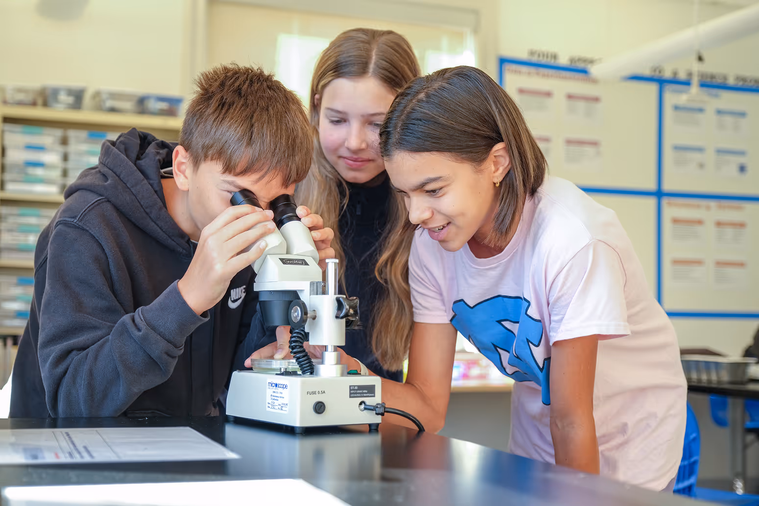 Cary Academy middle school students using a microscope to explore specimens in science lab class.