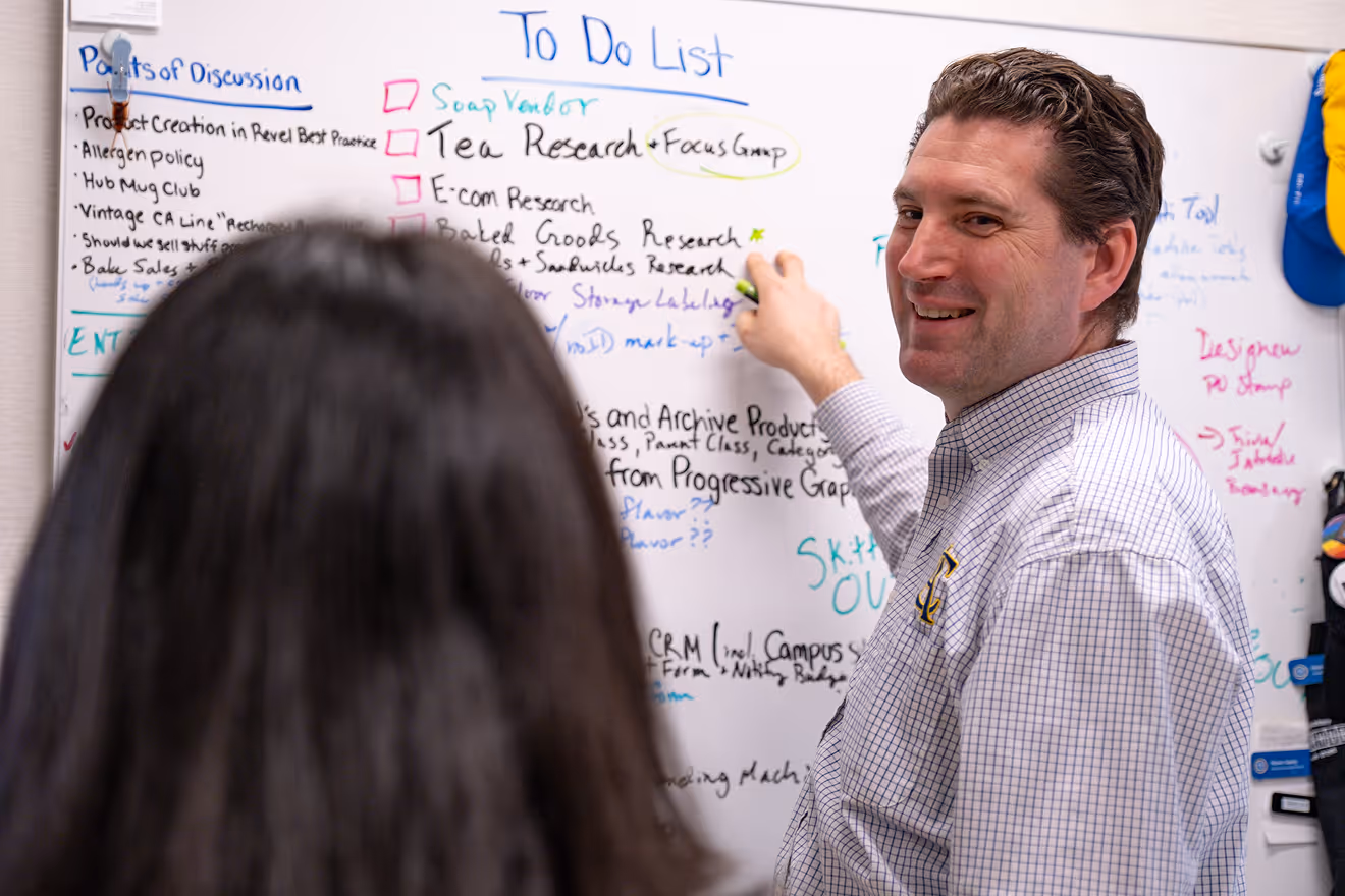 Cary Academy teacher leading classroom discussion while writing on whiteboard during business and entrepreneurship class.