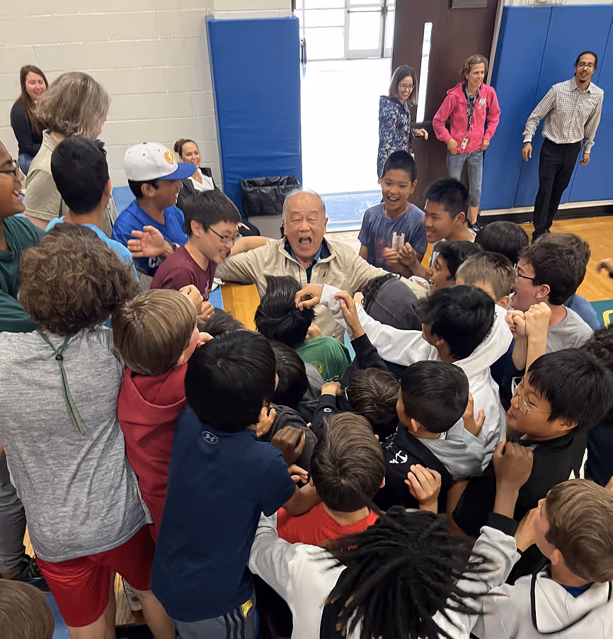 Cary Academy students surrounding and cheering with a teacher during a joyful assembly in the gym.