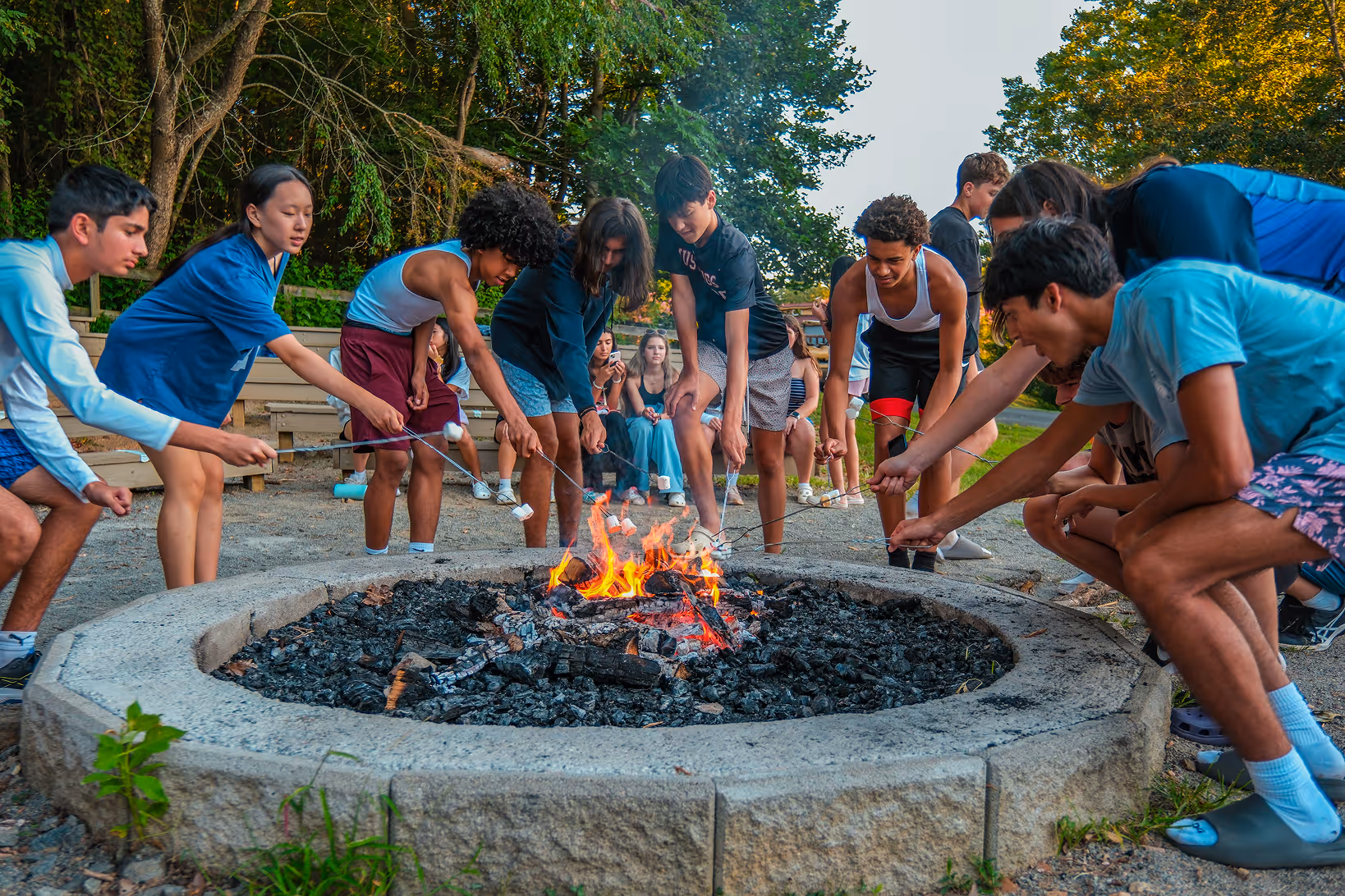 Cary Academy 9th grade students roasting marshmallows around a campfire during class trip outdoor activity.