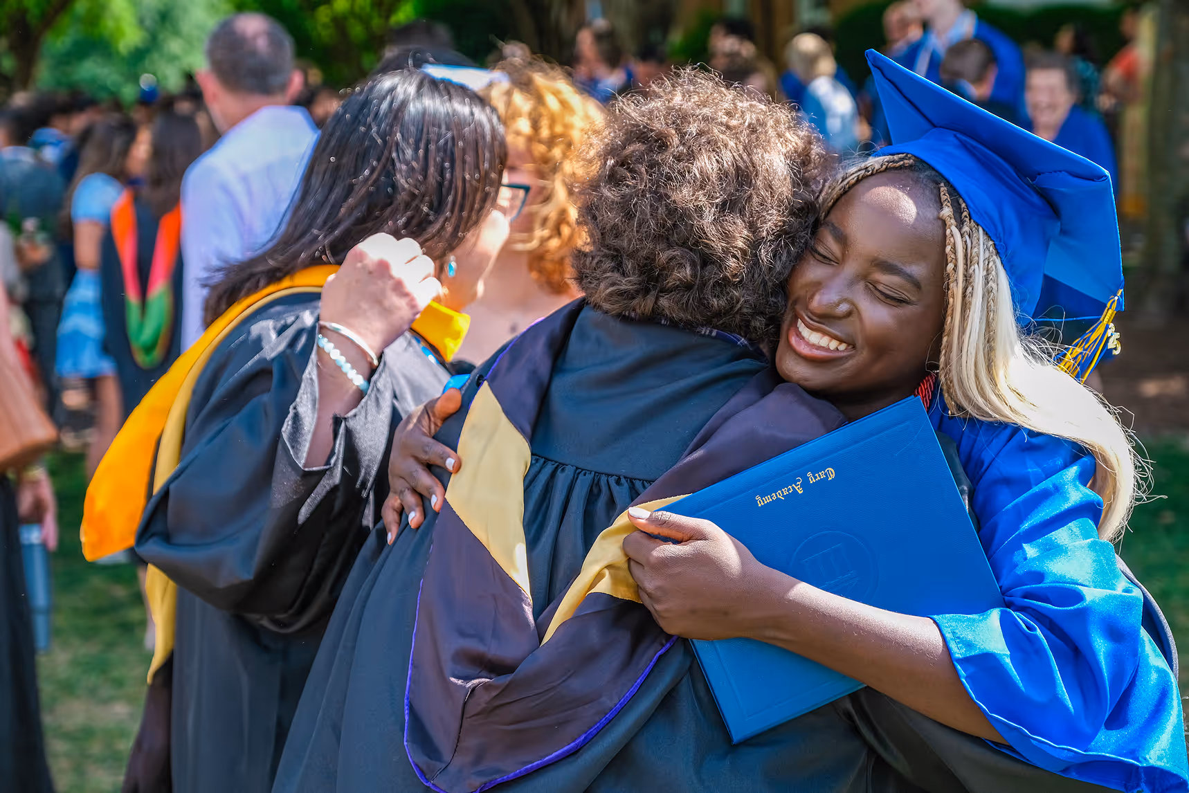 Cary Academy graduate hugging teacher during 2025 commencement celebration while holding diploma.