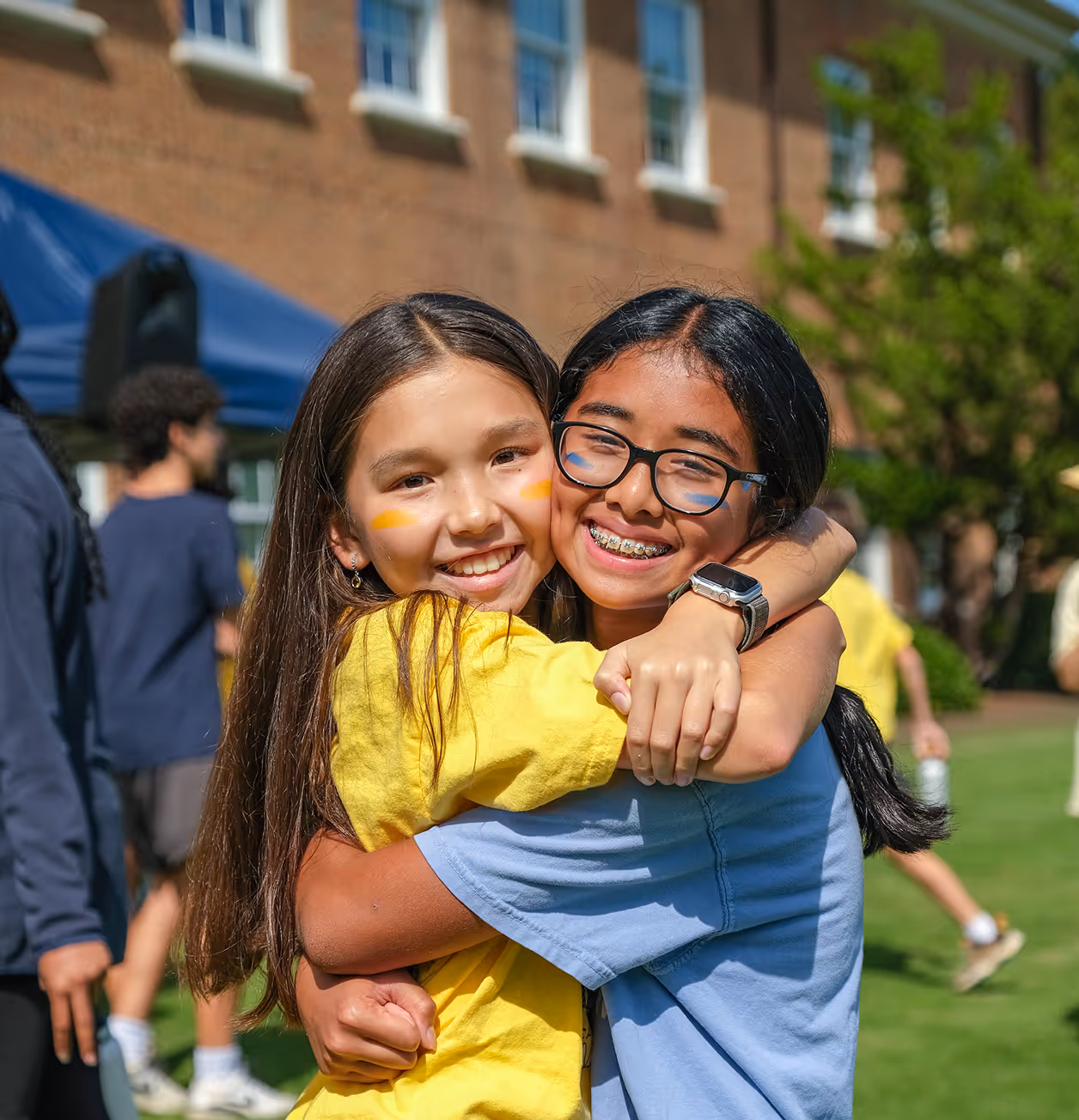 Cary Academy students hugging and smiling outdoors during Charger Cup school spirit event.