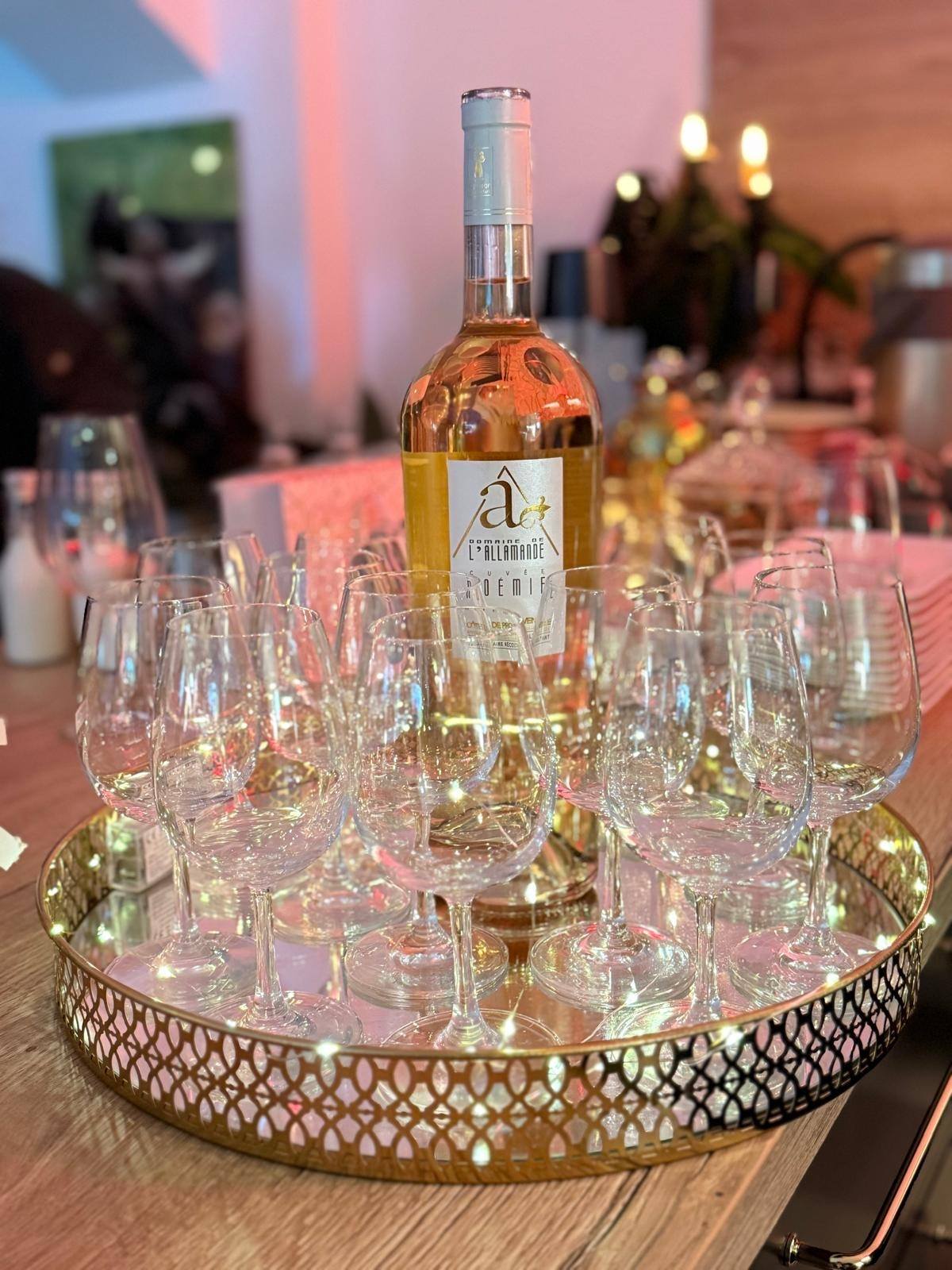 Bottle of rosé wine surrounded by empty wine glasses arranged on a decorative gold tray on a wooden table.