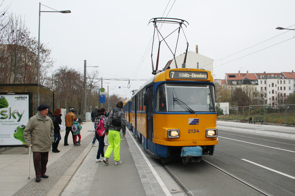 Yellow and blue tram number 7 at a station with people waiting and walking nearby on a cloudy day.