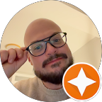 Man with glasses and a beard touching his glasses, with an orange star icon in the lower right corner.