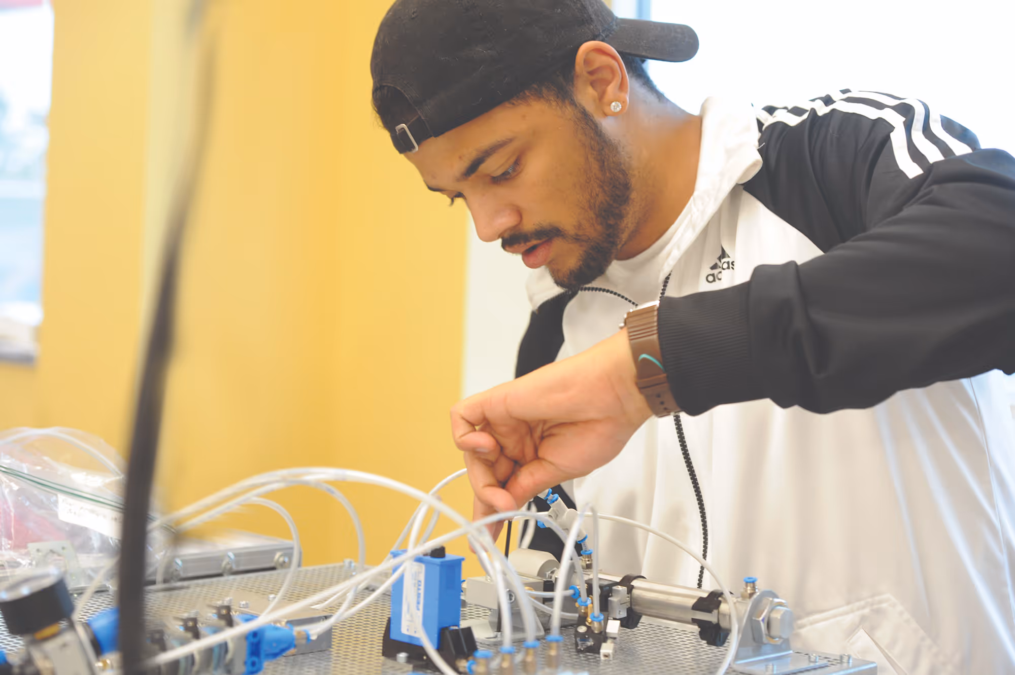 Male student in college science lab adjusting tubes on a mechanical apparatus.