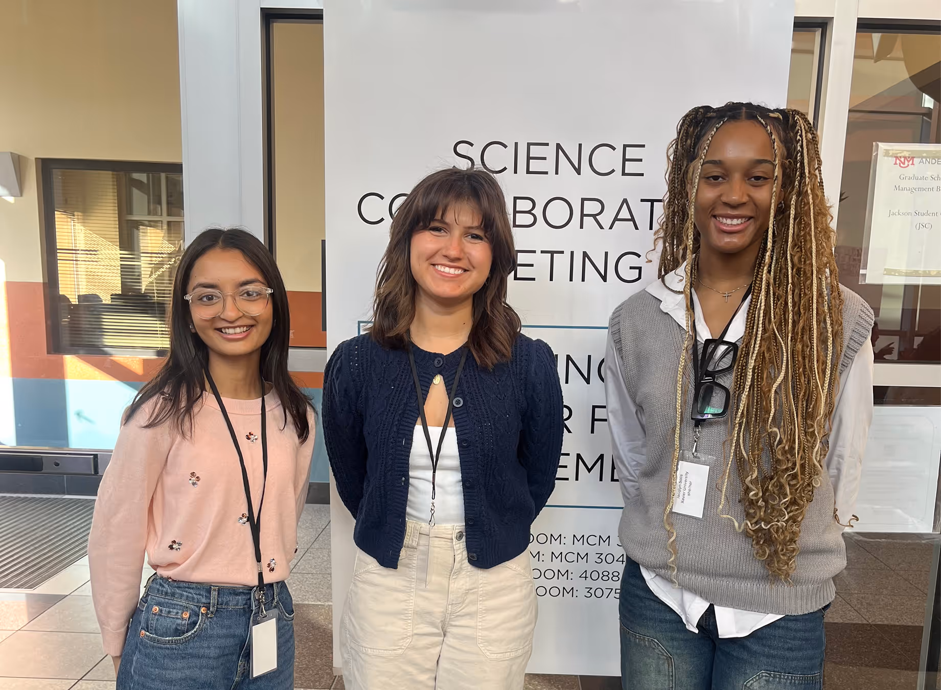 Three students in front of a sign about science collaboration meetings.