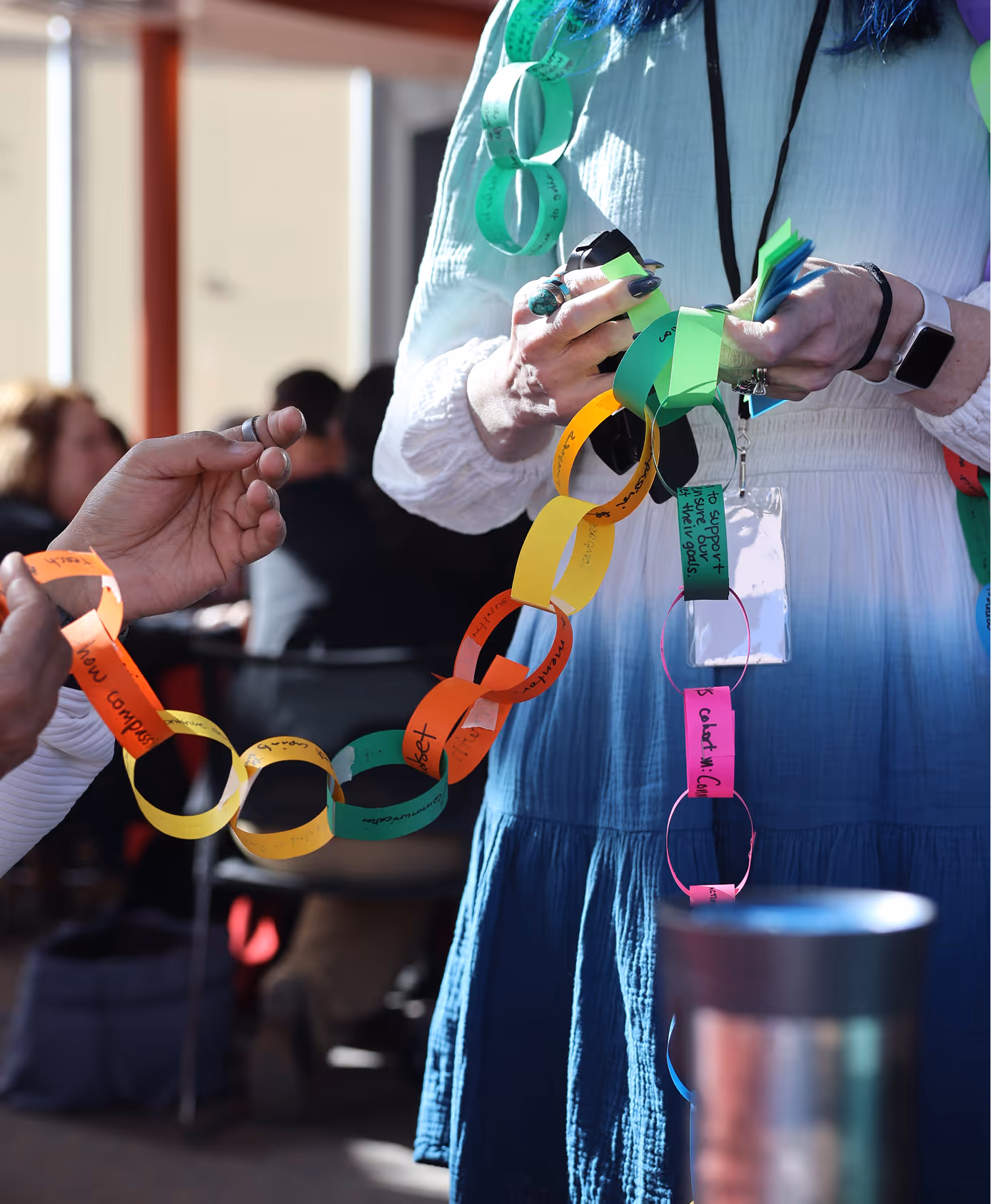 Two people holding and linking colorful paper chains with handwritten notes in a bright room.