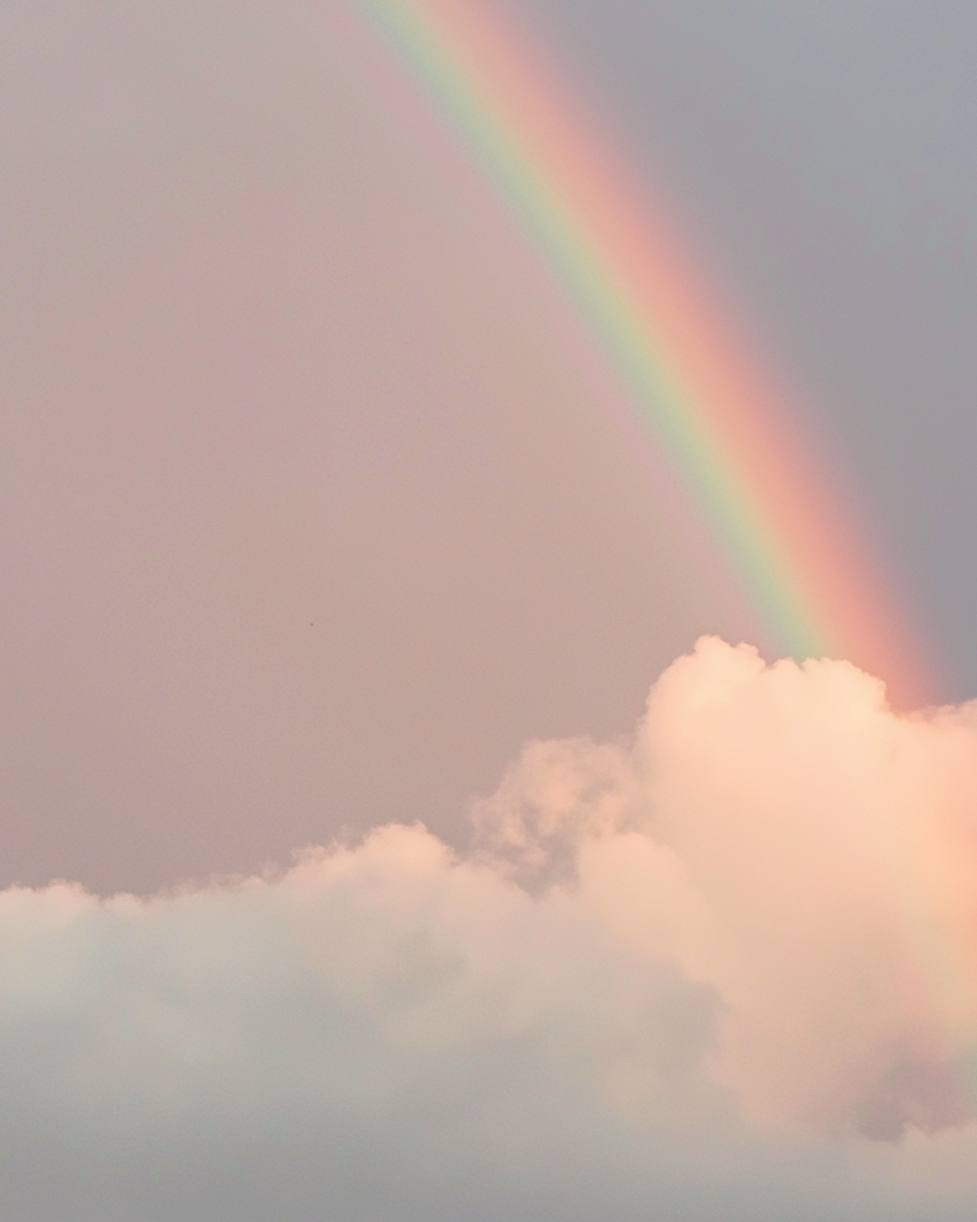 Soft rainbow arching over fluffy clouds against a pastel sky.
