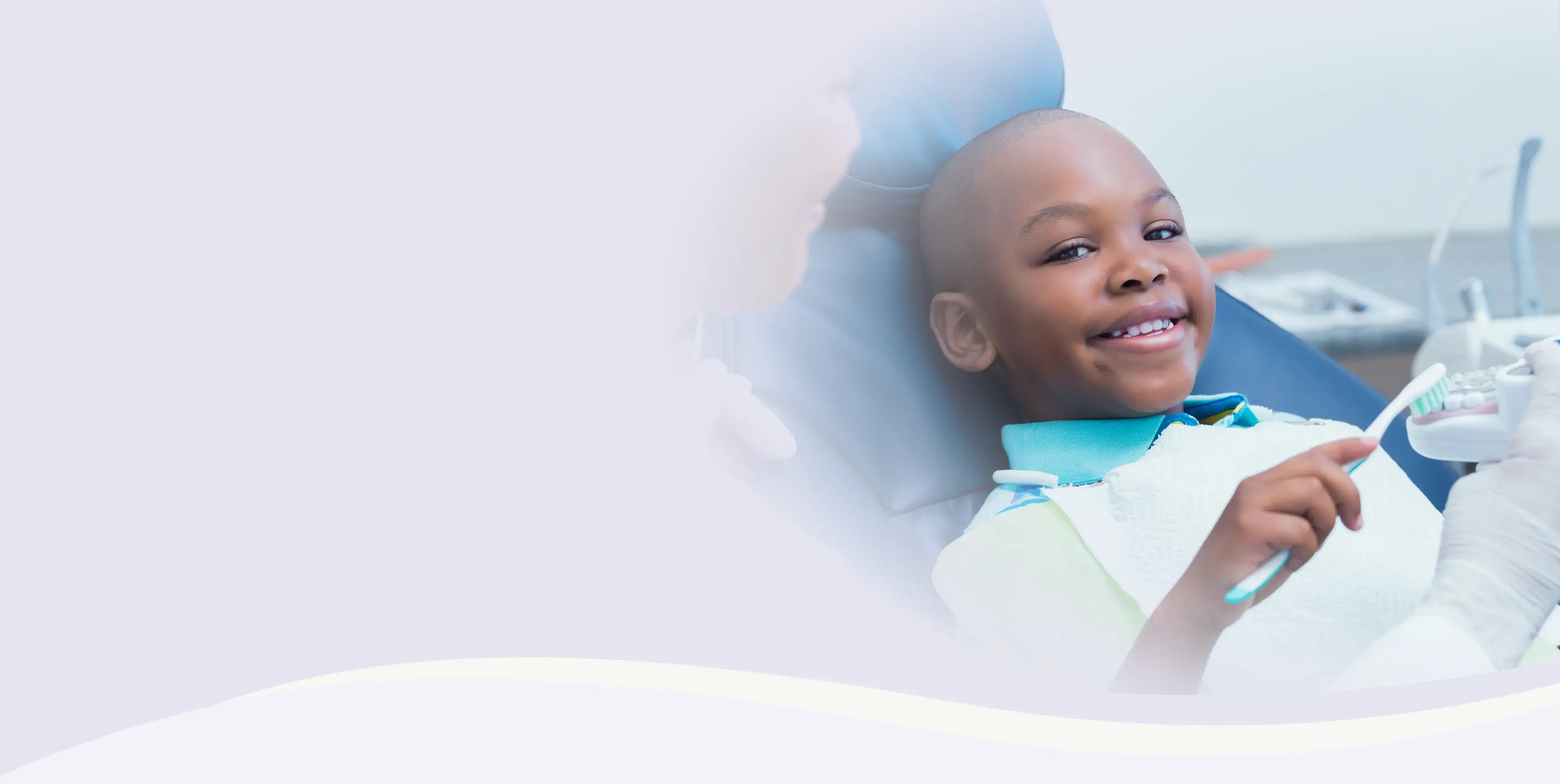 A child sits in a dental chair, smiling, while holding a toothbrush.
