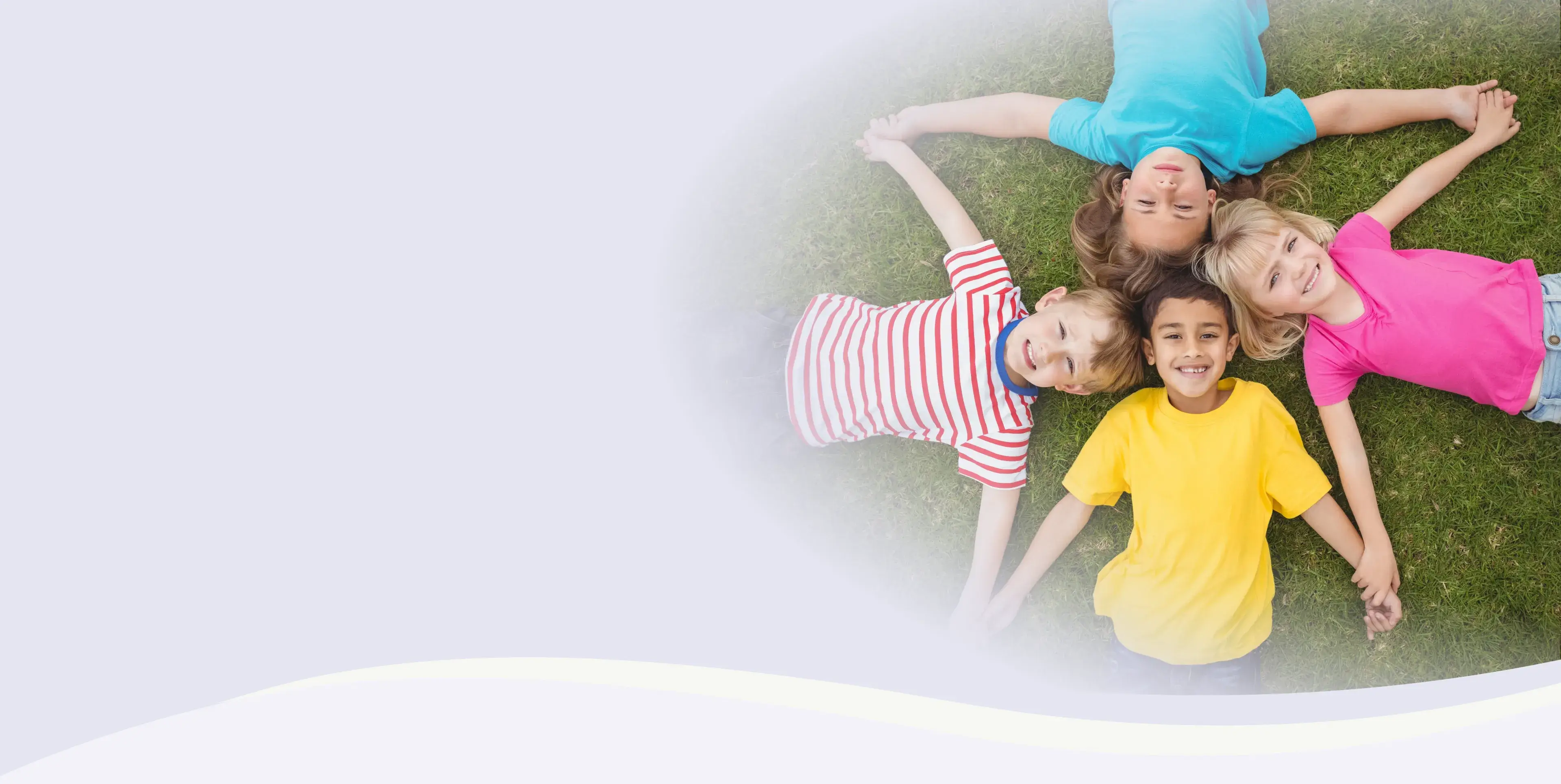 Four children lying on grass hold hands and smile upwards.