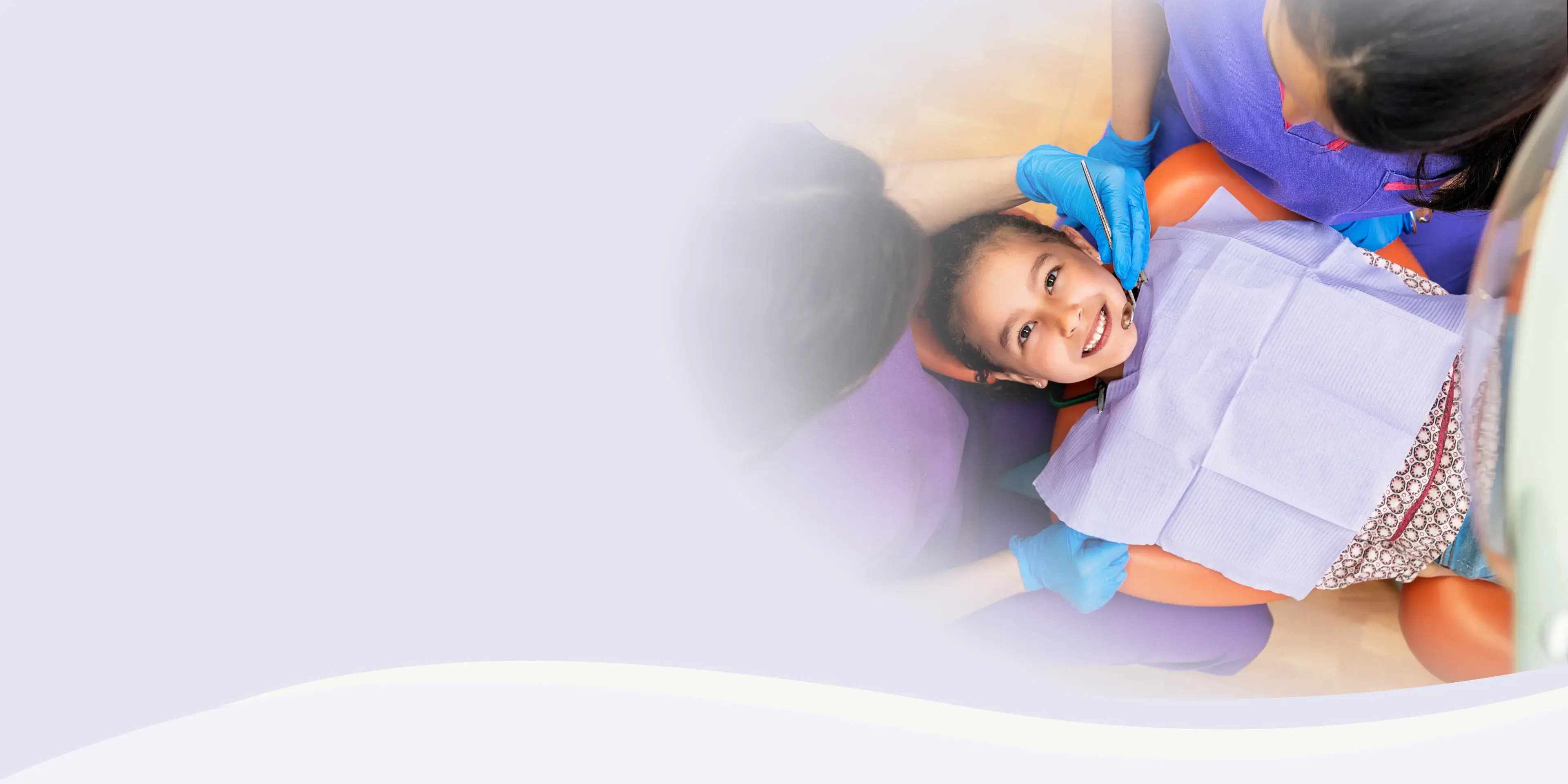 Child sitting in a dental chair, smiling, with a dental hygienist wearing gloves assisting them.