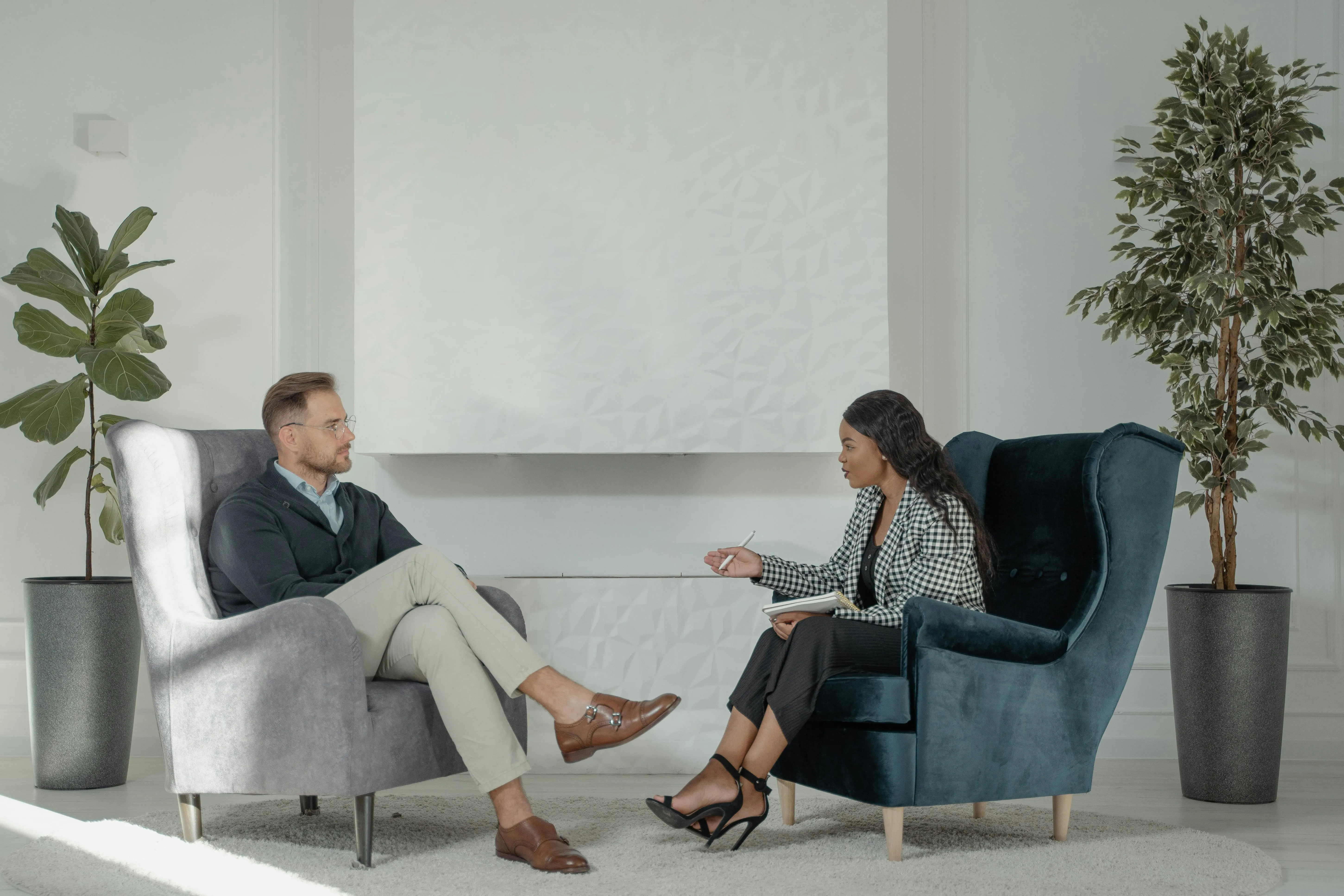 Man and woman seated in armchairs facing each other having a conversation in a modern, minimalist room.