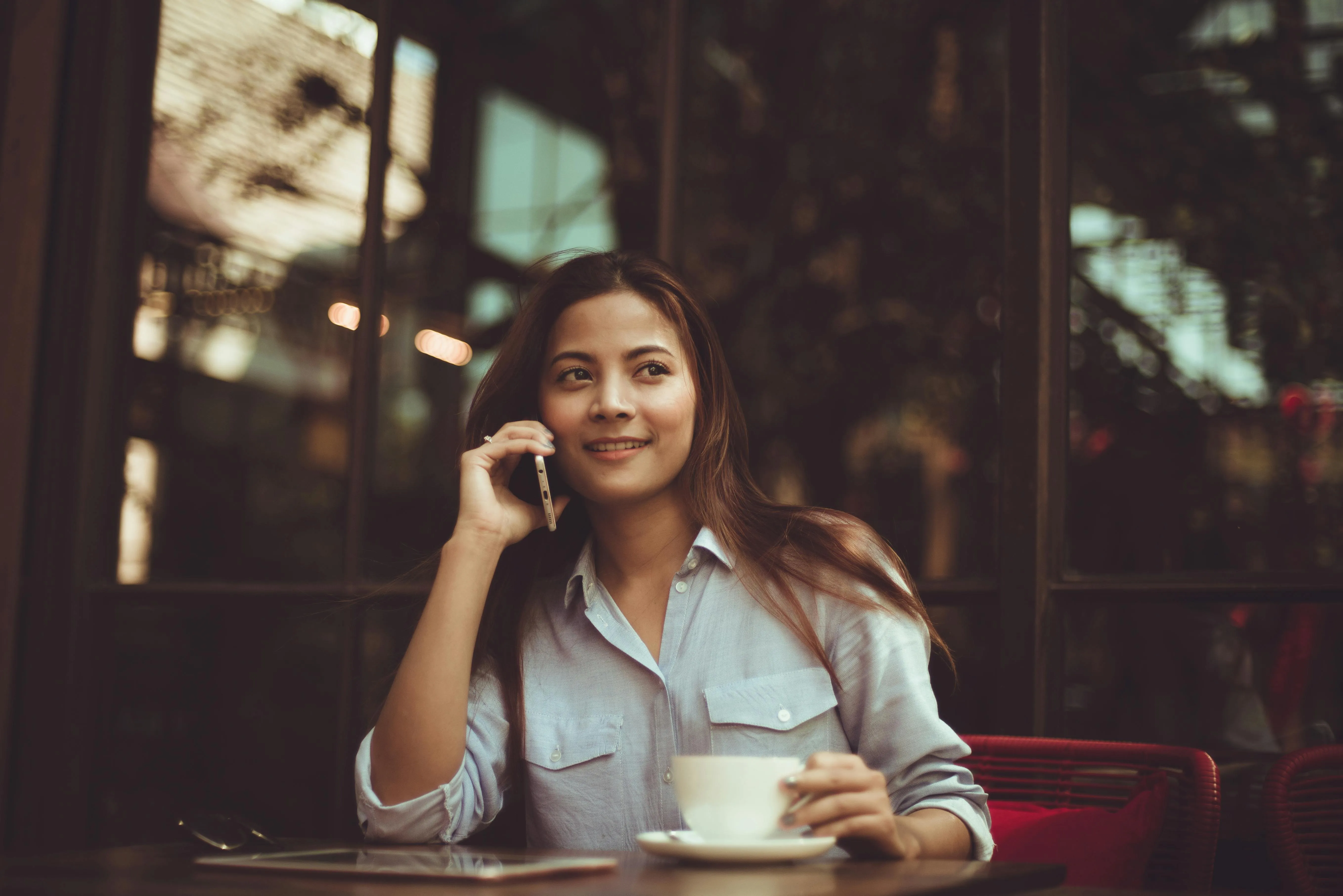 Young woman smiling while talking on the phone and holding a cup in a cozy café.