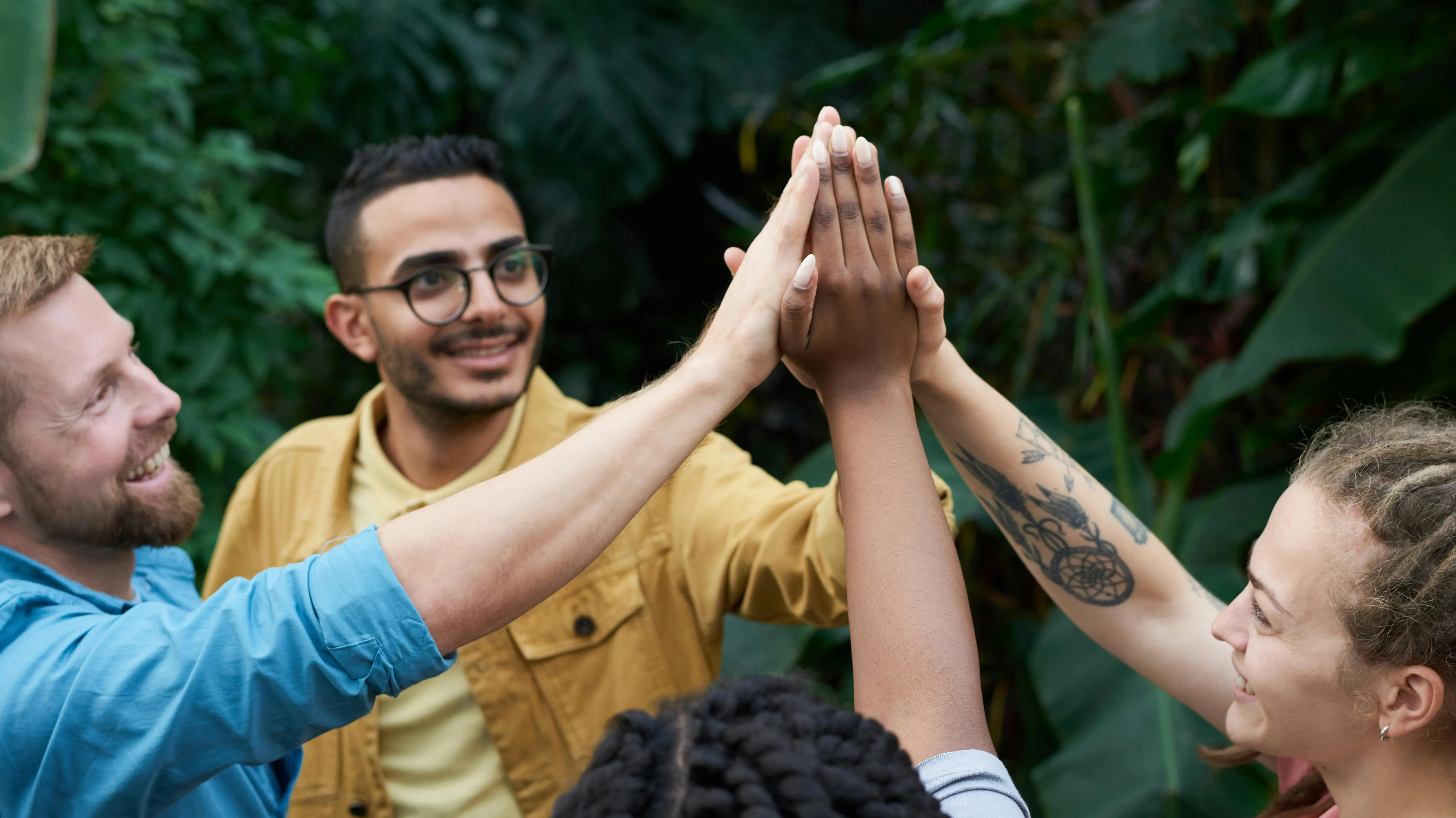 Four diverse friends outdoors smiling and giving a group high-five.