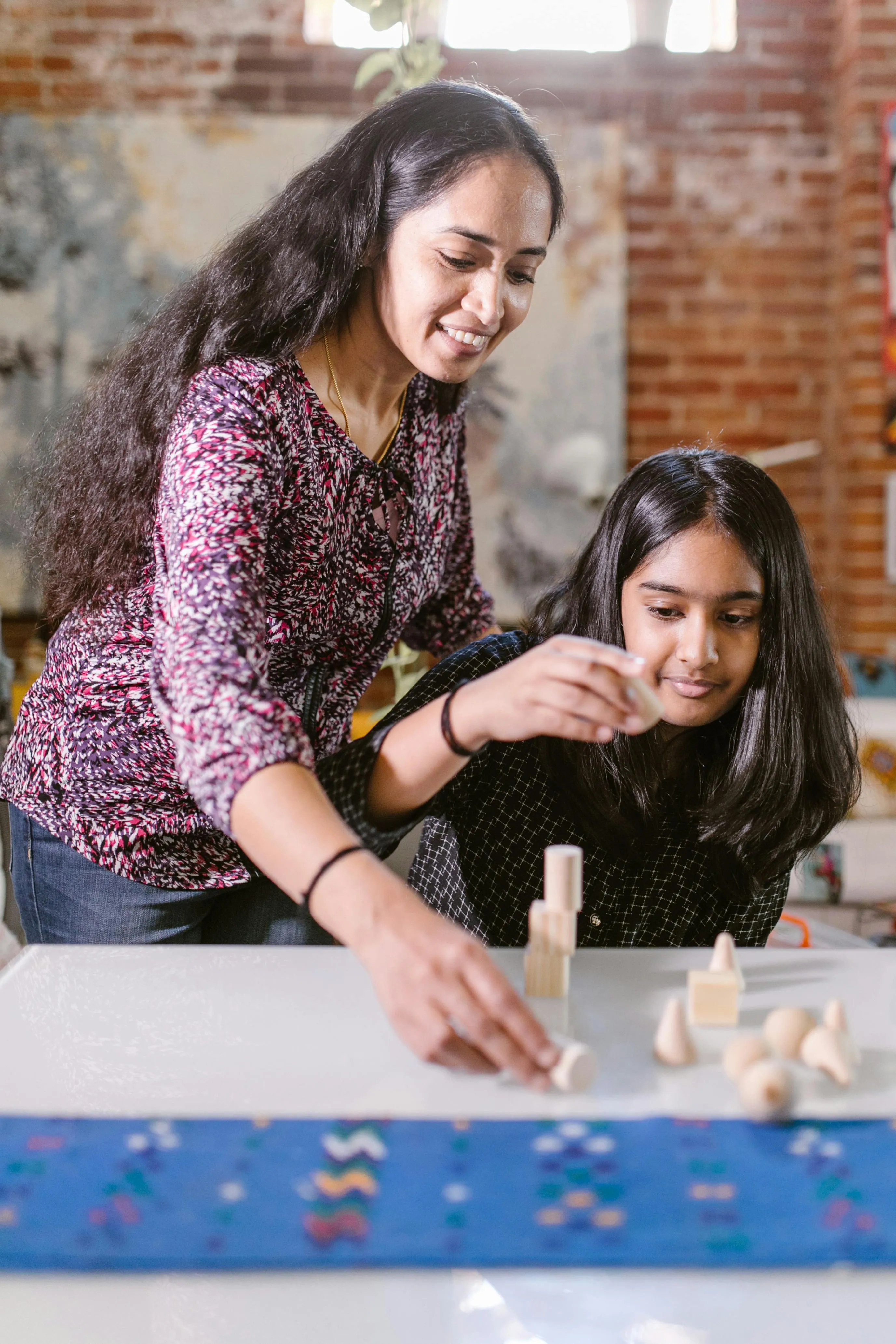 Woman and girl playing with wooden geometric blocks on a white table indoors.